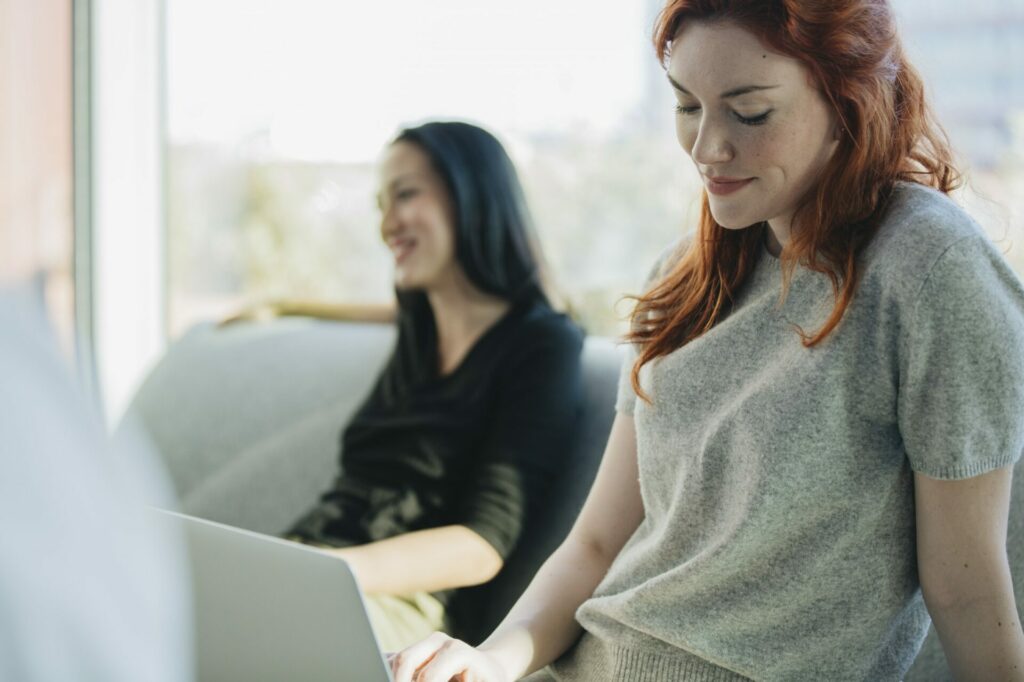 2 femmes assisent dont l'une regarde son ordinateur
